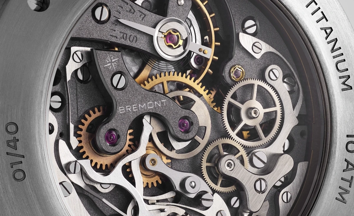 Yakından çekilen bu görselde, Bremont Altitude Chronograph Pulsograph saatinin Valjoux 23 kronograf mekanizması, gümüş ve altın renkli karmaşık dişliler, mor yakutlar ve detaylı köprüler ile zarif bir şekilde sergilenirken, kasada TITANIUM ve 01/40 seri numarası görülüyor.