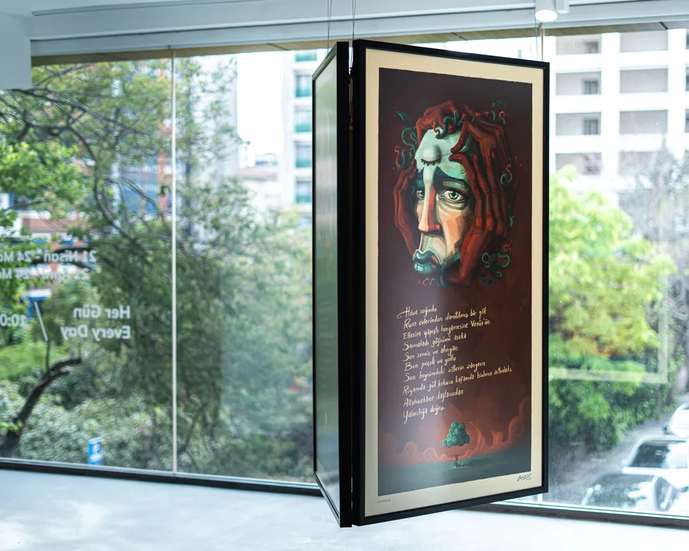 Decollage Sanat Alanı'nda sergilenen Onur Erler'in eserinde, kulaklarını elleriyle kapatmış, melankolik ifadeli stilize bir yüz ve altında kaligrafik metinlerle küçük bir ağaç figürü, koyu kırmızı arka plan üzerinde siyah bir çerçeveyle, dışarıdaki yeşil şehir manzarasını yansıtan büyük bir pencerenin önünde asılı duruyor.