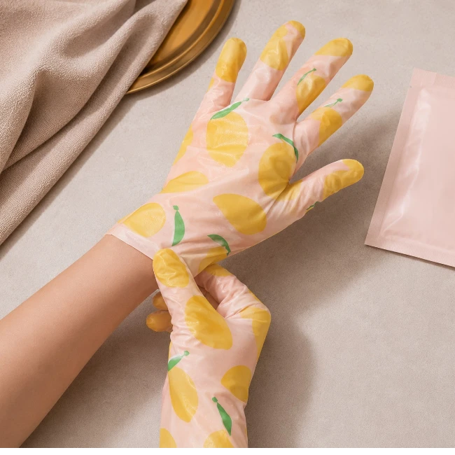 Sol elde sarı mango desenleriyle süslenmiş şeffaf pembe bir el maskesi eldiveni takılıyken, sağ elin bu eldiveni bilekten nazikçe ayarlayarak kusursuz bir el maskesi uygulaması için hazırlandığı bu görsel, eller için yoğun bir bakım anını vurguluyor.