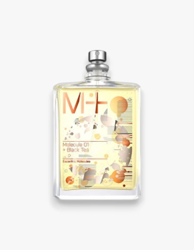 Dikdörtgen şeffaf cam şişede, sarımsı bir sıvı içeren Escentric Molecules Molecule 01 + Black Tea parfümü, metalik gümüş püskürtücüsü ve turuncu-altın M+ logosuyla dikkat çekiyor; etiketindeki soyut desenler modern ve zarif bir görünüm sunuyor.