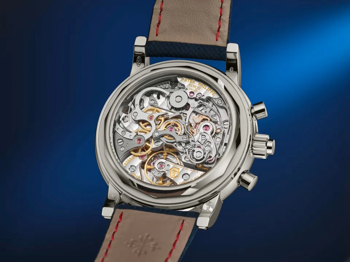 Mavi bir arka plan üzerinde, Patek Philippe Ref. 5204G modelinin şeffaf arka kapağından görünen, karmaşık çarklar, yaylar ve yakutlarla dolu, sonsuz takvim ve ayrık saniye kronograf gibi yüksek komplikasyonlara sahip gümüş tonlu bir mekanizma tüm ayrıntılarıyla sergileniyor.
