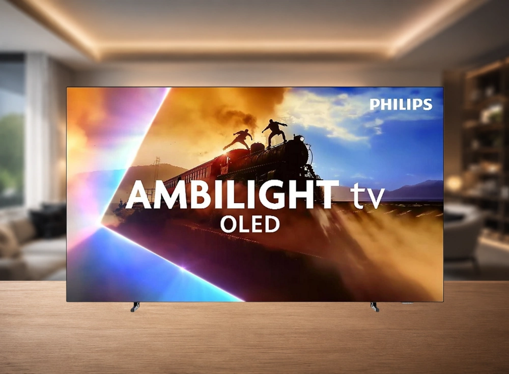 Philips marka bir OLED akıllı televizyon, ekranında iki kişinin tren üzerinde atladığı dinamik ve renkli bir aksiyon sahnesi gösteriyor; bu sahne, AMBILIGHT ve OLED yazılarıyla vurgulanırken, televizyon modern bir oturma odası düzeninde ahşap bir yüzeyde yer alıyor.