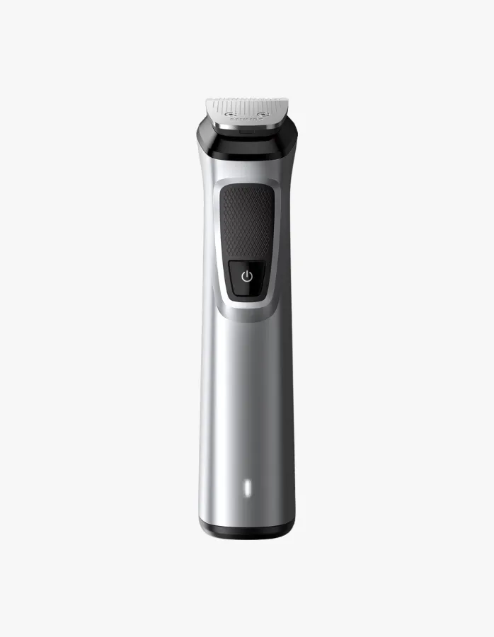 Dikey konumda, beyaz bir arka plan üzerinde duran, gümüş ve siyah renklerdeki Philips Multigroom Series 7000 erkek bakım cihazı, açma/kapama düğmesi ve alt kısmında yanan beyaz şarj gösterge ışığıyla detaylı bir şekilde sergileniyor.