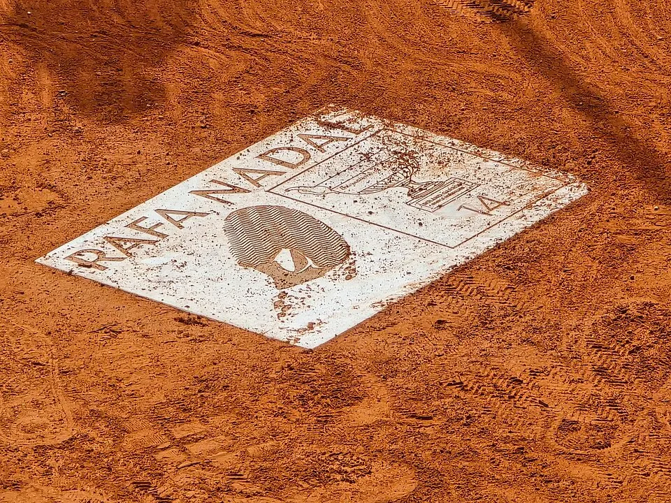 Kırmızı Roland Garros toprak kortuna gömülü, üzerinde RAFA NADAL yazısı, ikonik boğa logosu, kupası ve 14 şampiyonluğunu simgeleyen sayıyla Rafael Nadal'ın eşsiz zaferlerini kutlayan beyaz bir plaket.