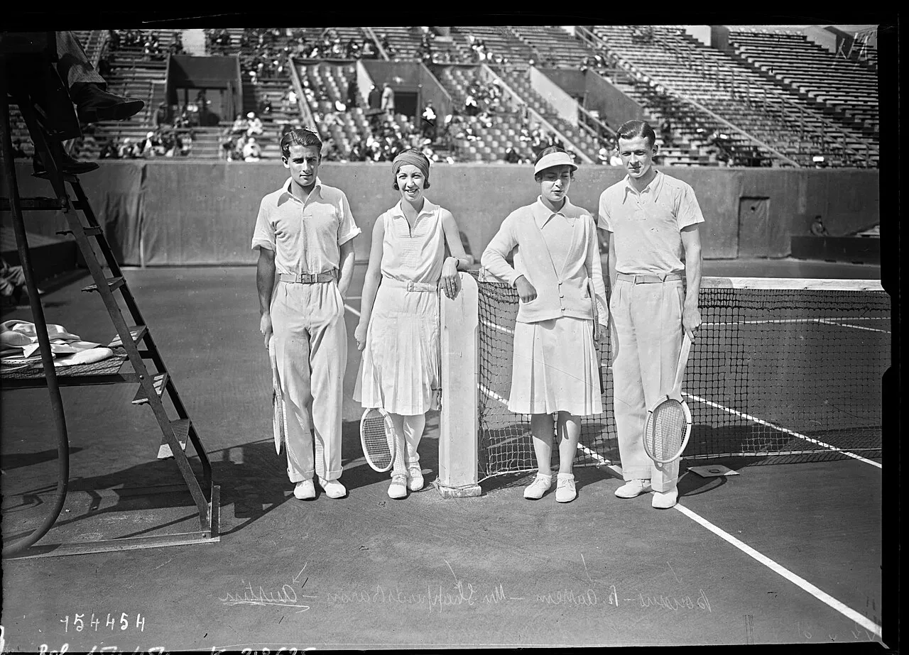 Büyük, siyah beyaz bir fotoğrafta, tenis kortunda ağın yanında, raketleriyle poz veren, dönemin tenis kıyafetleri içindeki iki erkek ve iki kadın tenisçi görünüyor; arka planda tribünlerdeki seyircilerle birlikte, bu görüntü Roland Garros Fransız Şampiyonası'nın ilk dönemlerinden bir anı yansıtıyor.