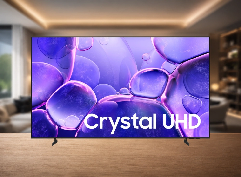 Ahşap bir yüzey üzerinde konumlanmış 55 inçlik Samsung 4K LED akıllı TV, ekranında mor ve mavi renkte saydam kabarcıkların ve beyaz Crystal UHD yazısının yer aldığı dikkat çekici bir görselle modern bir yaşam alanında sunuluyor.