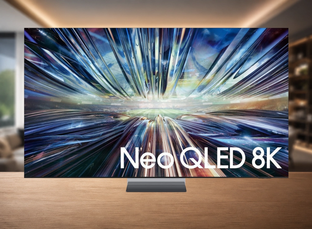 Masa üzerinde duran, çerçevesiz tasarıma sahip, Neo QLED 8K yazılı büyük Samsung televizyonun ekranında mavi ve gümüş tonlarında soyut, hareketli çizgilerle dolu bir görüntü belirgin bir şekilde yer alıyor, bu da TV'nin gelişmiş görüntü kalitesini vurguluyor.