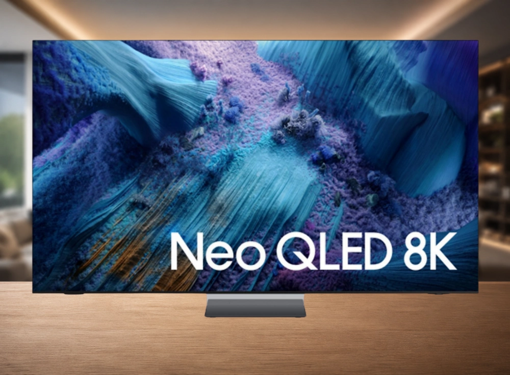 Bir ahşap sehpa üzerinde konumlandırılmış, canlı mavi ve mor tonlarda soyut bir desen ve Neo QLED 8K yazısı içeren ekranıyla dikkat çeken, zarif ve ince çerçeveli Samsung televizyon, üst düzey bir 8K mini LED sinema televizyonu olarak kablosuz bağlantı kutusu gibi özelliklere sahip olduğunu gösteriyor.