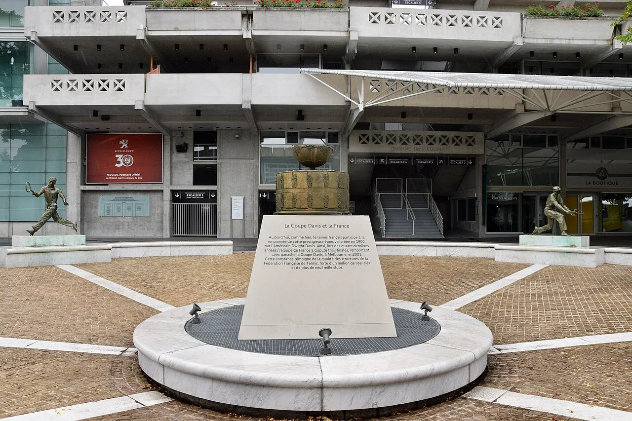 Stade Roland Garros'un beton ve modern mimarili giriş alanında, ortasında La Coupe Davis et la France yazılı kupa formunda bir anıt ve iki yanında tenisçileri betimleyen bronz heykellerin bulunduğu geniş bir meydan uzanıyor.