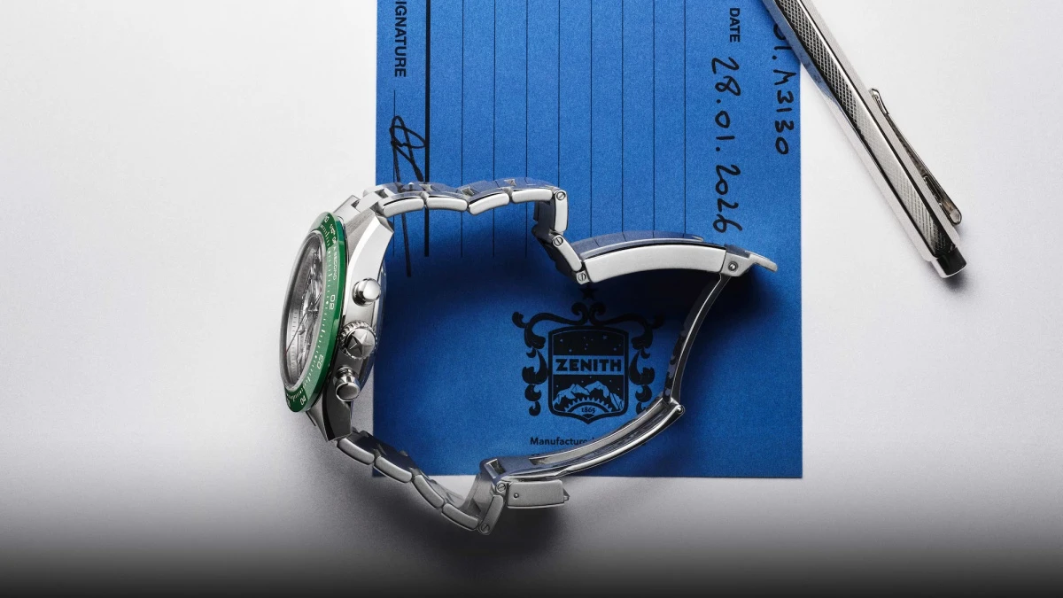 Zenith Chronomaster Sport Skeleton'ın Watches and Wonders 2026 etkinliği için dikkat çeken yeşil bezelli versiyonu, kadranındaki karmaşık iskelet mekanizması, açık tokalı metal bileziği ve kronograf butonlarıyla mavi bir dosya ile parlak metalik bir kalemin yanında estetik bir kompozisyon oluşturuyor.