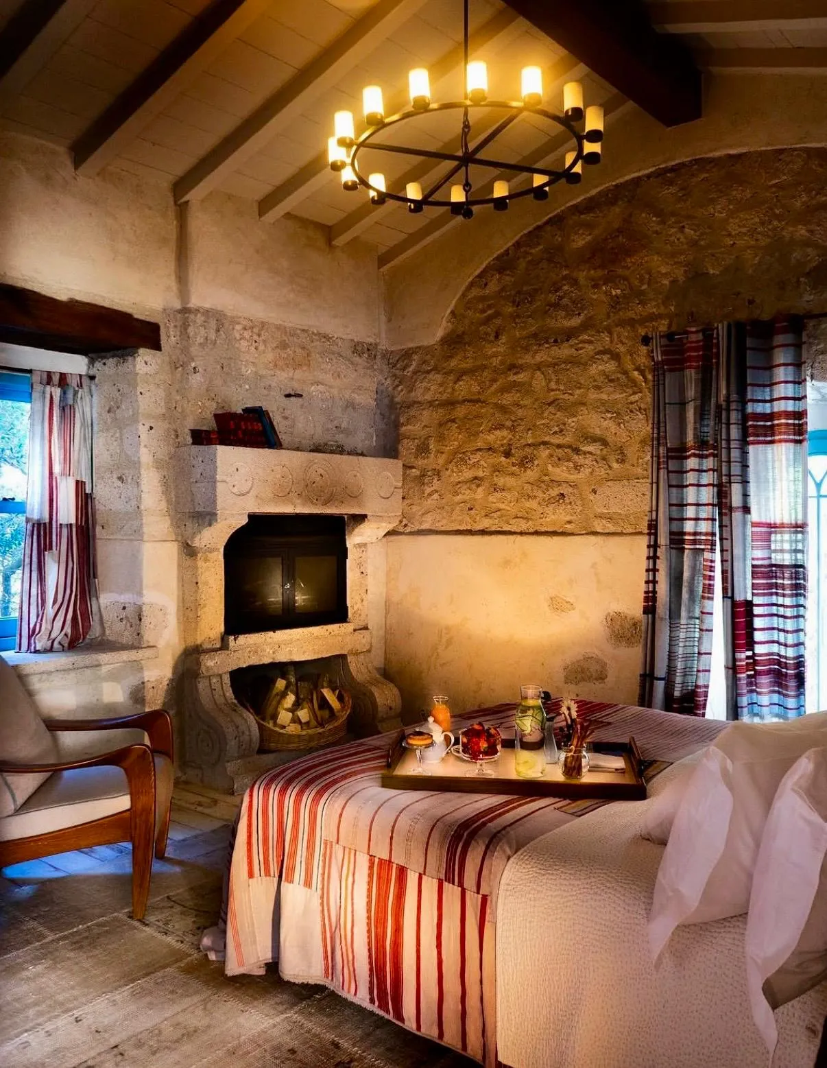 Alavya Otel'in geleneksel taş duvarlara, ahşap tavan kirişlerine ve modern aydınlatmaya sahip, yatak üzerinde kahvaltı tepsisi bulunan şömineli sıcak odası, huzurlu bir konaklama ortamı sunuyor.