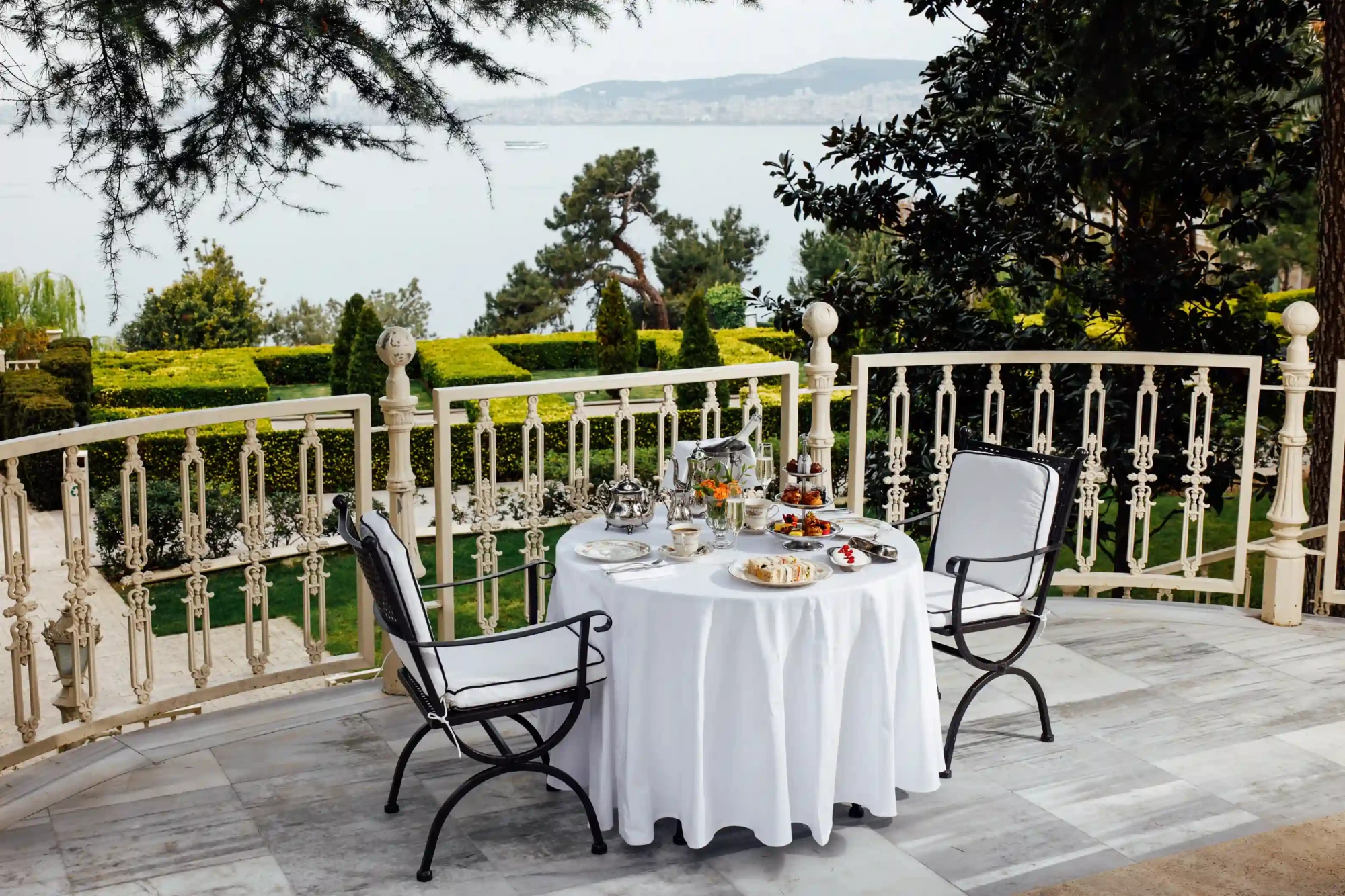 Arka planda Büyükada'nın ve denizin huzur veren manzarasının eşlik ettiği, beyaz örtülü şık bir masada Anneler Günü brunchı için özenle hazırlanmış enfes ikramlar ve zarif bir atmosfer sunan keyifli bir teras düzenlemesi.