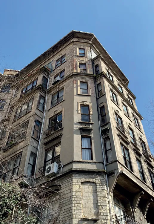 Mavi gökyüzü altında, çıplak ağaç dallarının çevrelediği, aşağıdan yukarıya doğru bakış açısıyla görüntülenen Arif Paşa Apartmanı, cephesindeki yer yer dökülmelerine rağmen köşeli mimarisi, demir balkonlu pencereleri ve yedi katlı heybetiyle dikkat çekiyor.