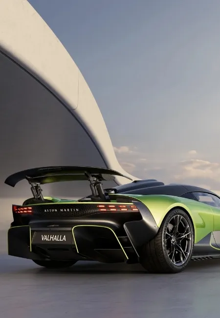 Arka planda modern bir mimari yapının ve açık havanın görüldüğü, beton zeminde duran, parlak yeşil Aston Martin Valhalla'nın arka görünümü, Formula 1 teknolojisinden ilham alan aktif aerodinamik tasarımı ve devasa arka kanadıyla markanın radikal hypercar kimliğini vurguluyor.