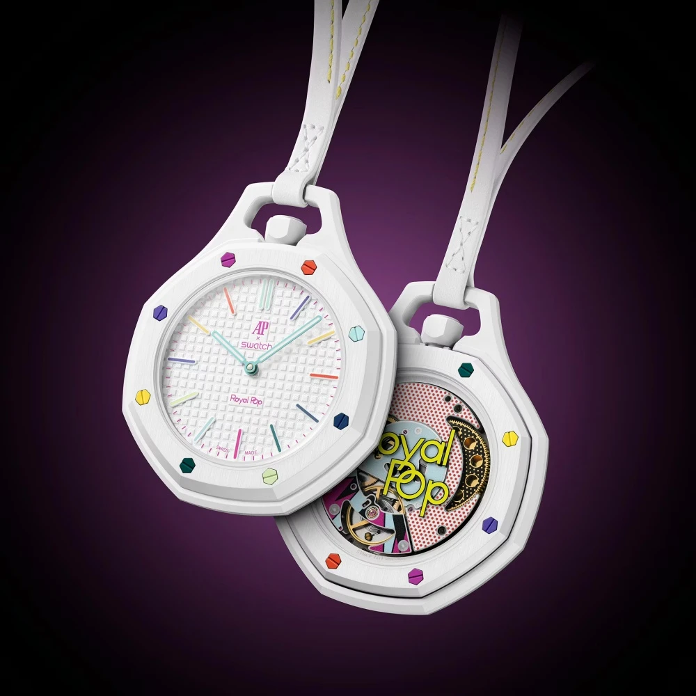 İki beyaz, sekizgen Audemars Piguet Swatch iş birliği Royal Pop cep saati, ön plandaki saat çok renkli indeksleri ve AP Swatch logosuyla kadranını gösterirken, arkadaki saat canlı pop-art tasarımlı mekanizmasını sergiliyor.
