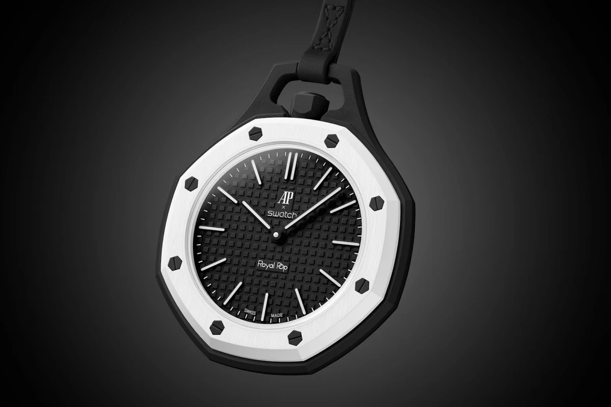 Koyu gri bir arka plan üzerinde hafifçe asılı duran, Audemars Piguet ve Swatch iş birliği ürünü olan, beyaz sekizgen çerçevesi, siyah ızgara desenli kadranı ve siyah askı detayıyla dikkat çeken Royal Pop cep saati modeli.