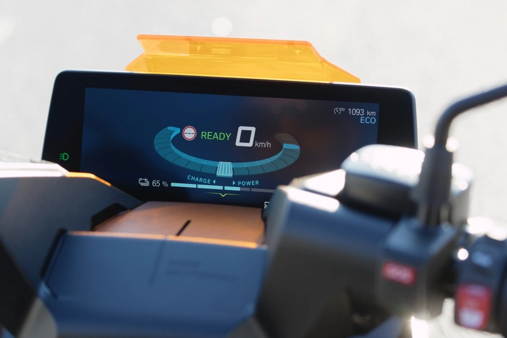 BMW CE 04 elektrikli scooter'ın modern dijital hayalet kadran ekranı yakından çekilmiş; pil şarjı, 0 km/s hızda hazır konumu, 1093 km toplam mesafe ve ECO sürüş modu bilgileri parlak mavi ve beyaz renklerle net bir şekilde görüntüleniyor.