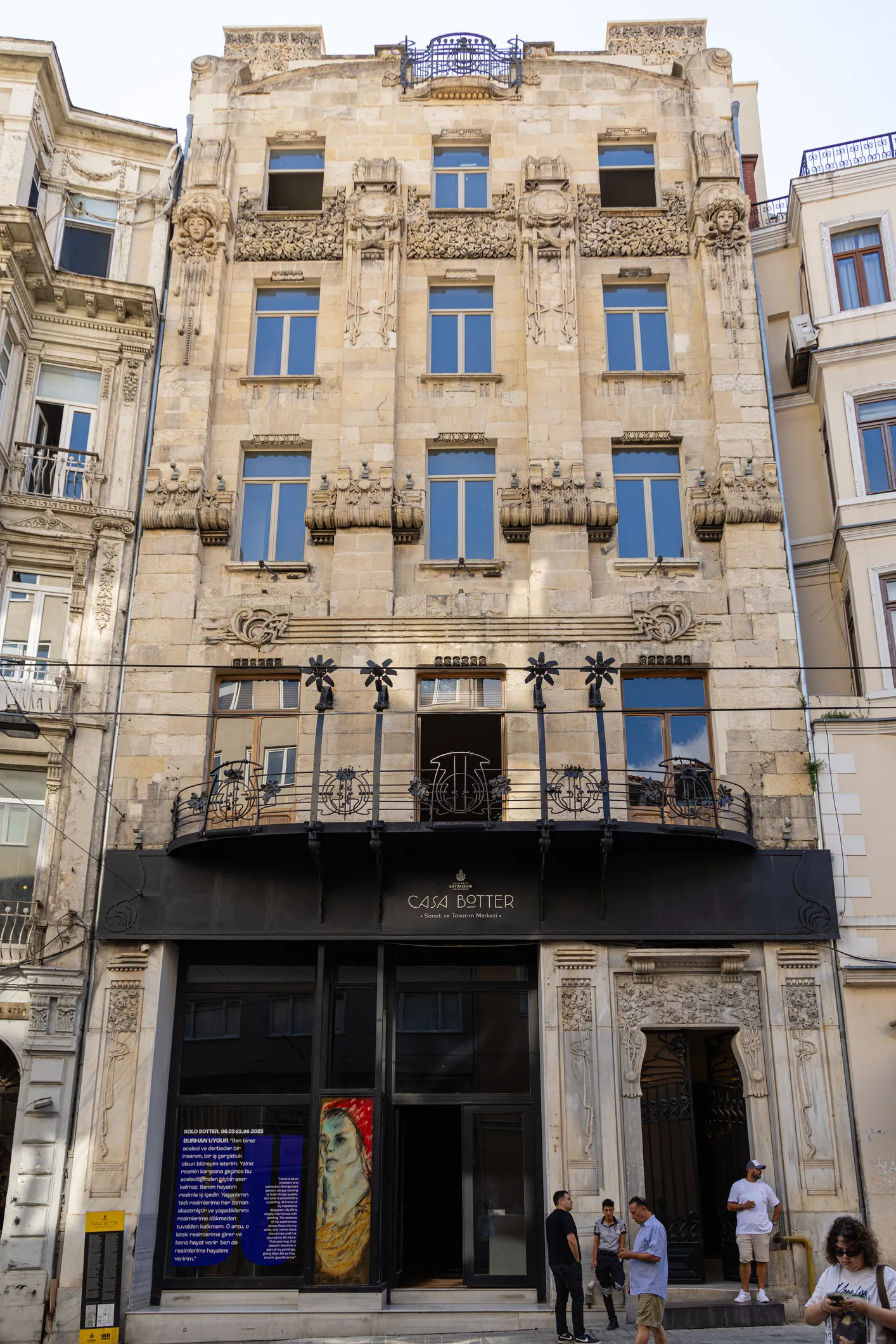 İstanbul'un tarihi yapılarından biri olan Botter Apartmanı'nın Art Nouveau mimarisiyle süslü, bej renkli taş cephesi, işlemeli pencere ve balkon korkulukları, zemin katında yer alan Casa Botter Sanat ve Tasarım Merkezi tabelası ve sergi vitriniyle birlikte caddeden çekilmiş detaylı bir fotoğrafı.