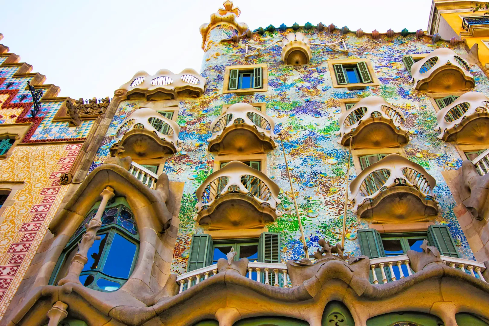 Casa Batlló'nun alt açıyla çekilmiş bu görselinde, Gaudi'nin kendine özgü organik mimari tarzını yansıtan, denizden ilham alan rengarenk mozaiklerle kaplı cephesi ve iskelet benzeri, dalgalı formdaki balkonları ön plana çıkıyor.
