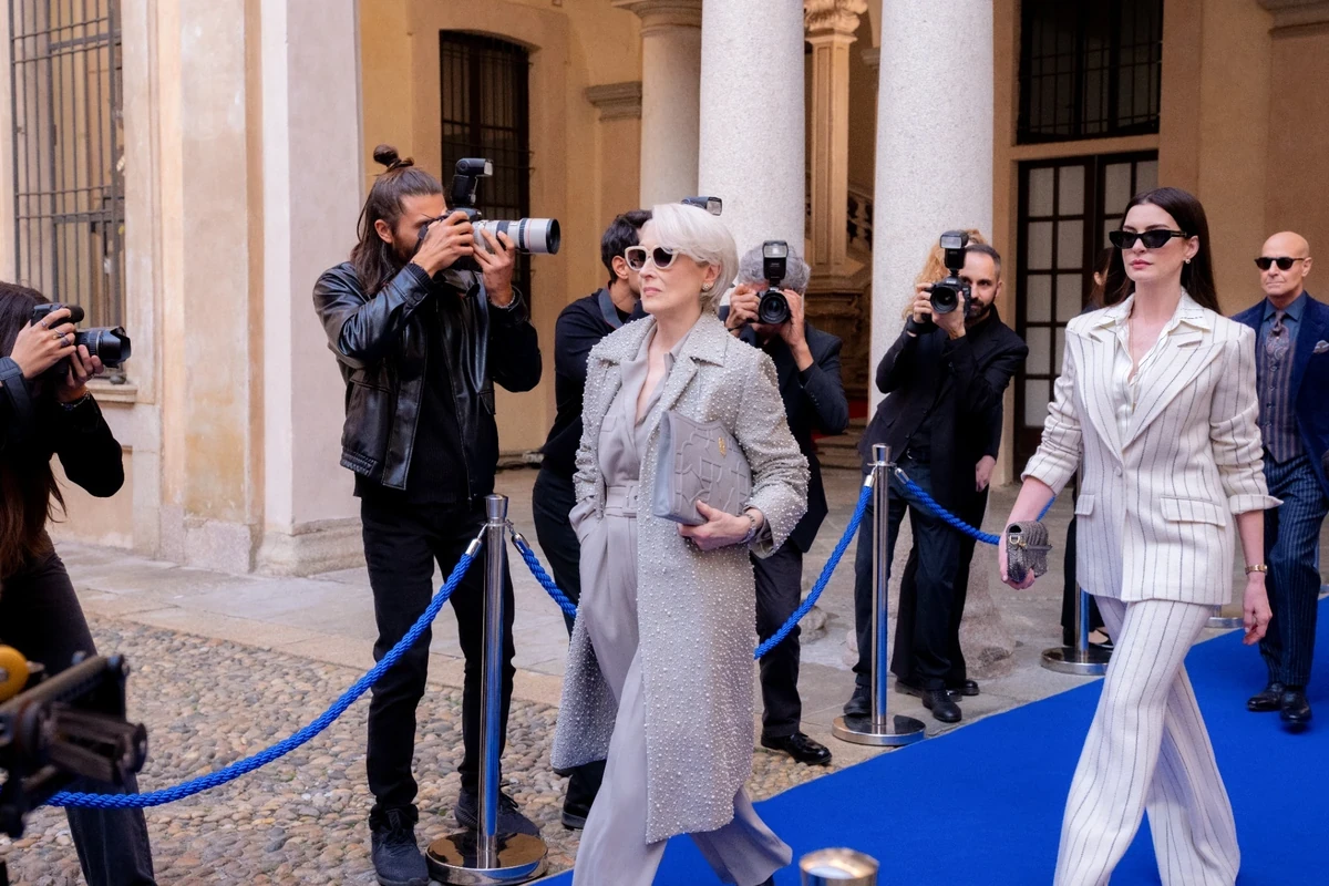 Miranda Priestly'yi canlandıran Meryl Streep gri işlemeli kabanıyla, Andy Sachs rolündeki Anne Hathaway ise zarif beyaz çizgili takımıyla The Devil Wears Prada 2'nin Milano'daki bir moda sahnesinde, çevrelerindeki flaşlar eşliğinde mavi halıda yürüyor.
