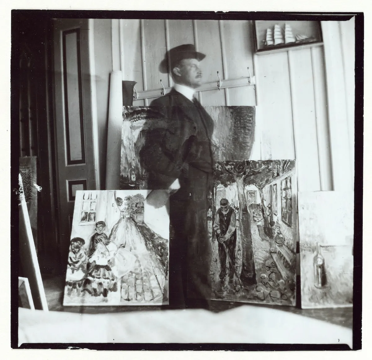 Siyah beyaz bir fotoğrafta, 1907 tarihli bir otoportrede, sanatçı Edvard Munch şapkalı ve takım elbiseli bir şekilde hafifçe silik bir görüntüyle odanın içinde ayakta duruyor ve önünde yerdeki üç Warnemünde tablosu belirgin bir şekilde görülüyor.