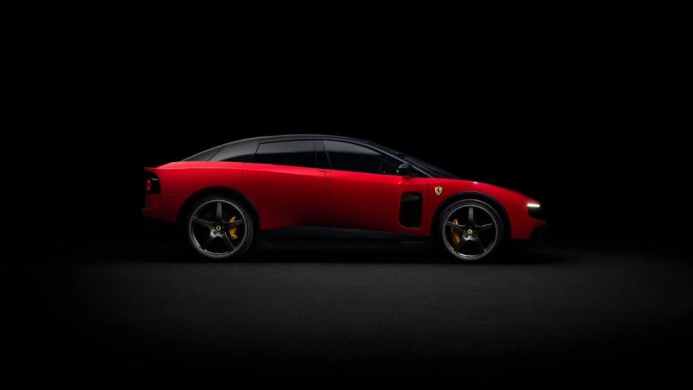 Karanlık bir zeminde, Jony Ive'ın imzasını taşıyan fütüristik ve sportif dış tasarıma sahip parlak kırmızı bir elektrikli Ferrari Luce modelinin yan profili, siyah tavanı, koyu renkli jantları ve sarı fren kaliperleriyle lüks ve yenilikçi bir duruş sergiliyor.