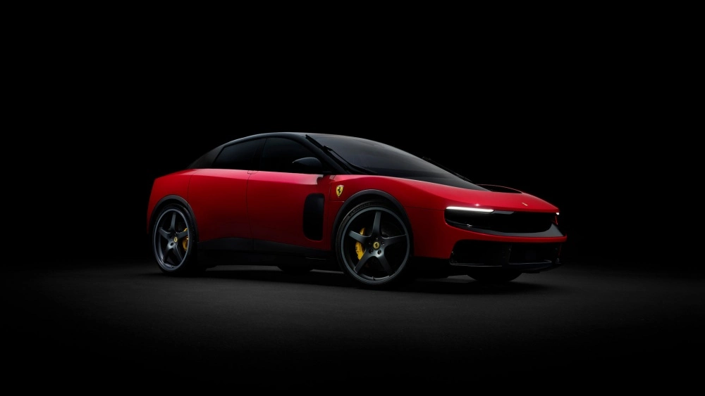Siyah bir stüdyo ortamında, modern ve aerodinamik dış tasarıma sahip, parlak kırmızı renkli ilk elektrikli Ferrari modeli Luce'nin ön ve yan profili çaprazdan vurgulu bir şekilde sergileniyor.