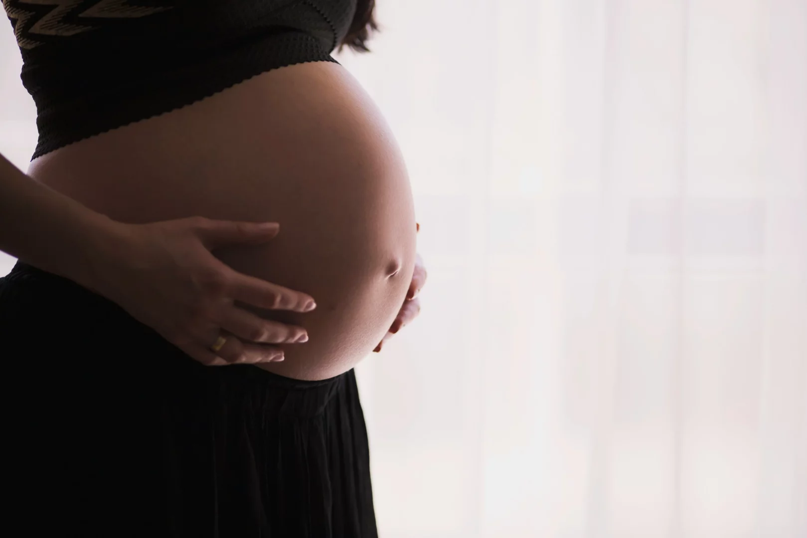Hamilelik sürecinde bebek sağlığı ve gelişimi için hayati öneme sahip folik asit takviyesinin faydalarını anlatan bu görselde, anne adayının elleriyle karnını şefkatle okşadığı yakın çekim bir an yansıtılıyor.