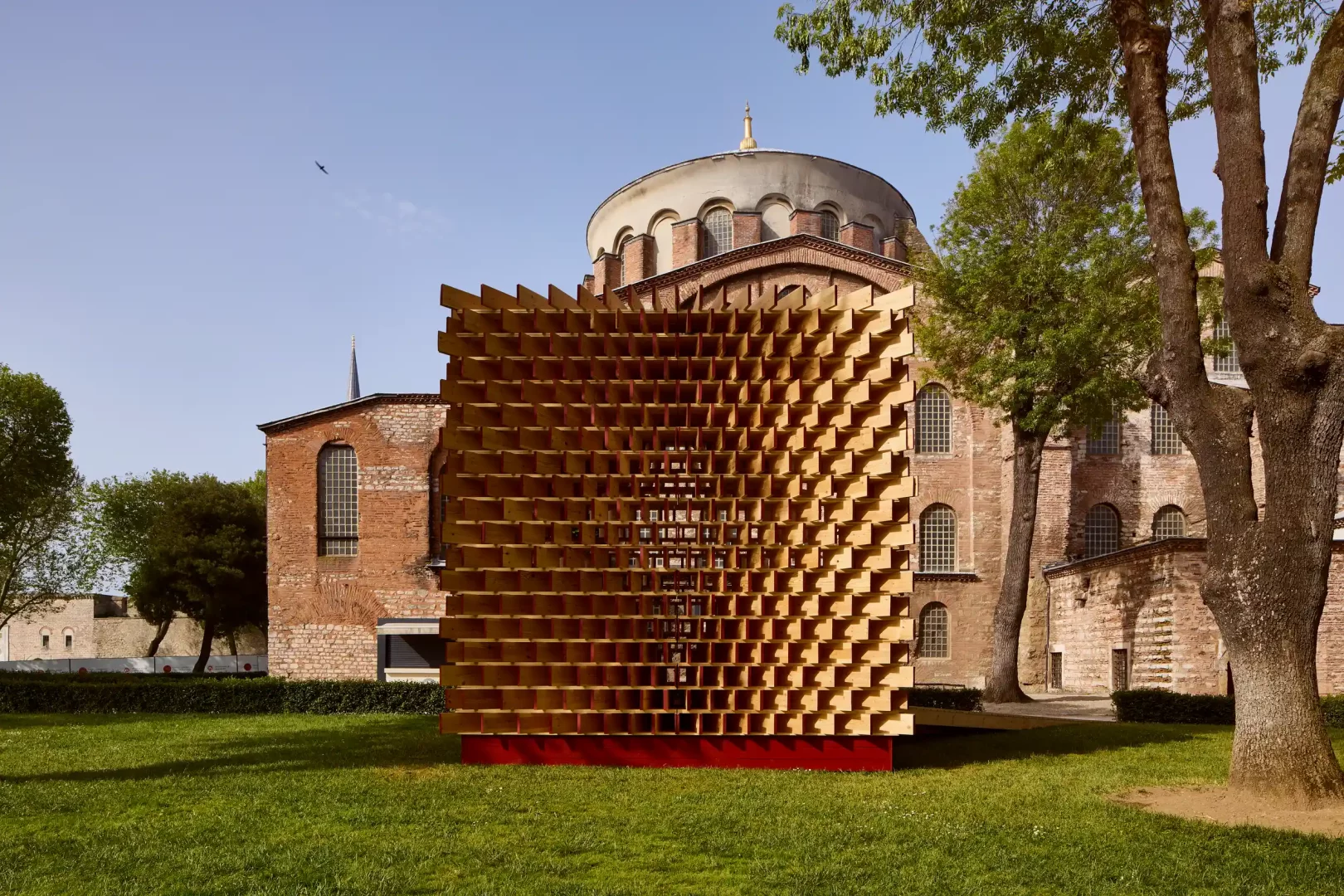 Aya İrini avlusundaki yemyeşil çimlerin üzerinde duran, Waugh Thistleton Architects tasarımı, kırmızı tabanlı, ahşap latalardan oluşan modern pavyon, Global Design Forum İstanbul'un Tasarım Bu Kez Şehre Yayılıyor konseptiyle kentin tarihi dokusunda yaratıcı bir kamusal yerleştirme olarak dikkat çekiyor.