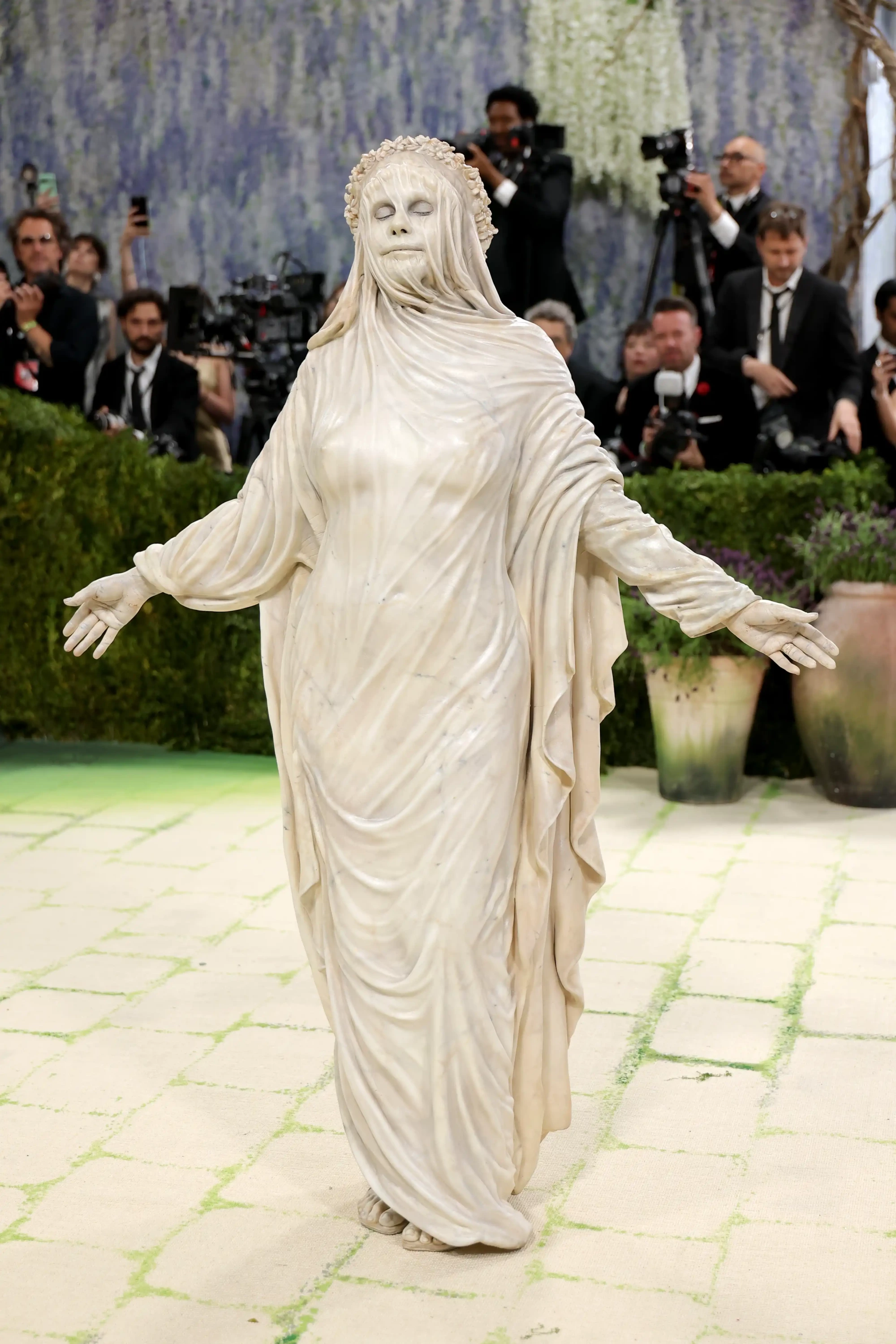 2026 Met Gala kırmızı halısında, heykelsi bir kostüm sanatı yaratıcılığıyla dikkat çeken Heidi Klum, mermer heykeli andıran drapeli, bej renkli, yüzü ve bedeni kumaşla örtülü, kolları açık ve zarif duruşuyla Fashion Is Art temasını mükemmel bir şekilde temsil ediyor.
