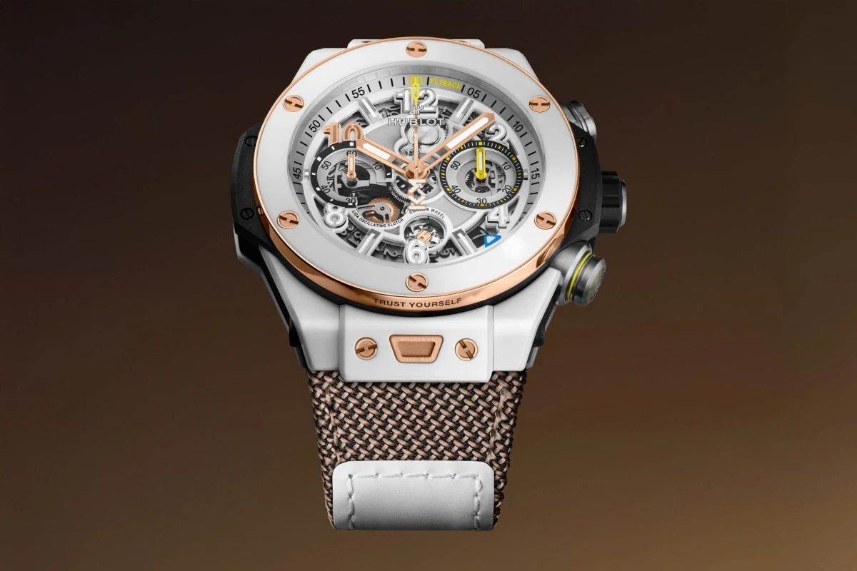 Hublot Big Bang Reloaded Kylian Mbappe sınırlı üretim kronograf saatin beyaz seramik kasası, iskelet kadranındaki pembe altın detayları ve sarı vurgularıyla dikkat çekici bir tasarıma sahip, kahverengi örgülü kayışıyla şık bir bütünlük sunuyor.