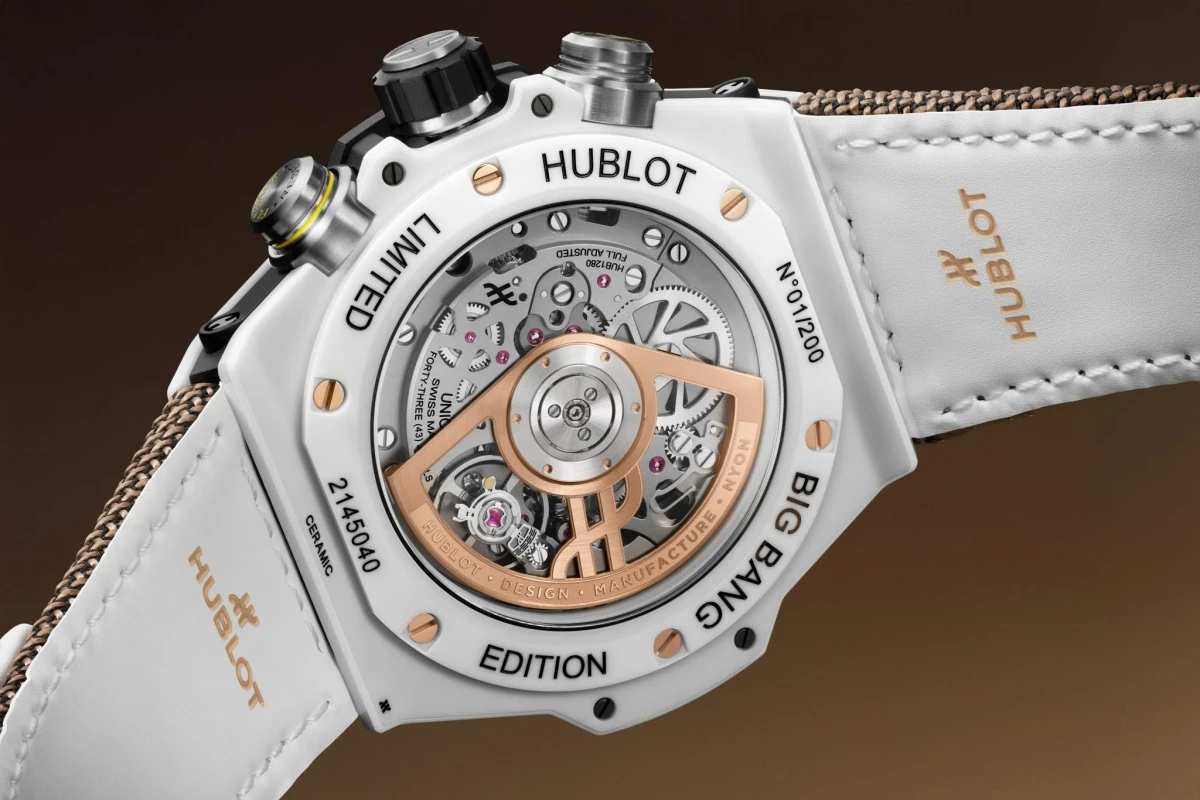Hublot Big Bang Kylian Mbappe özel serisi beyaz seramik saatin arkadan çekilen yakın plan görüntüsünde, karmaşık mekanik kronograf saat mekanizması ve üzerindeki rose gold rotor detayları, beyaz deri kordon ile sınırlı üretim ibareleri net bir şekilde görülebiliyor.