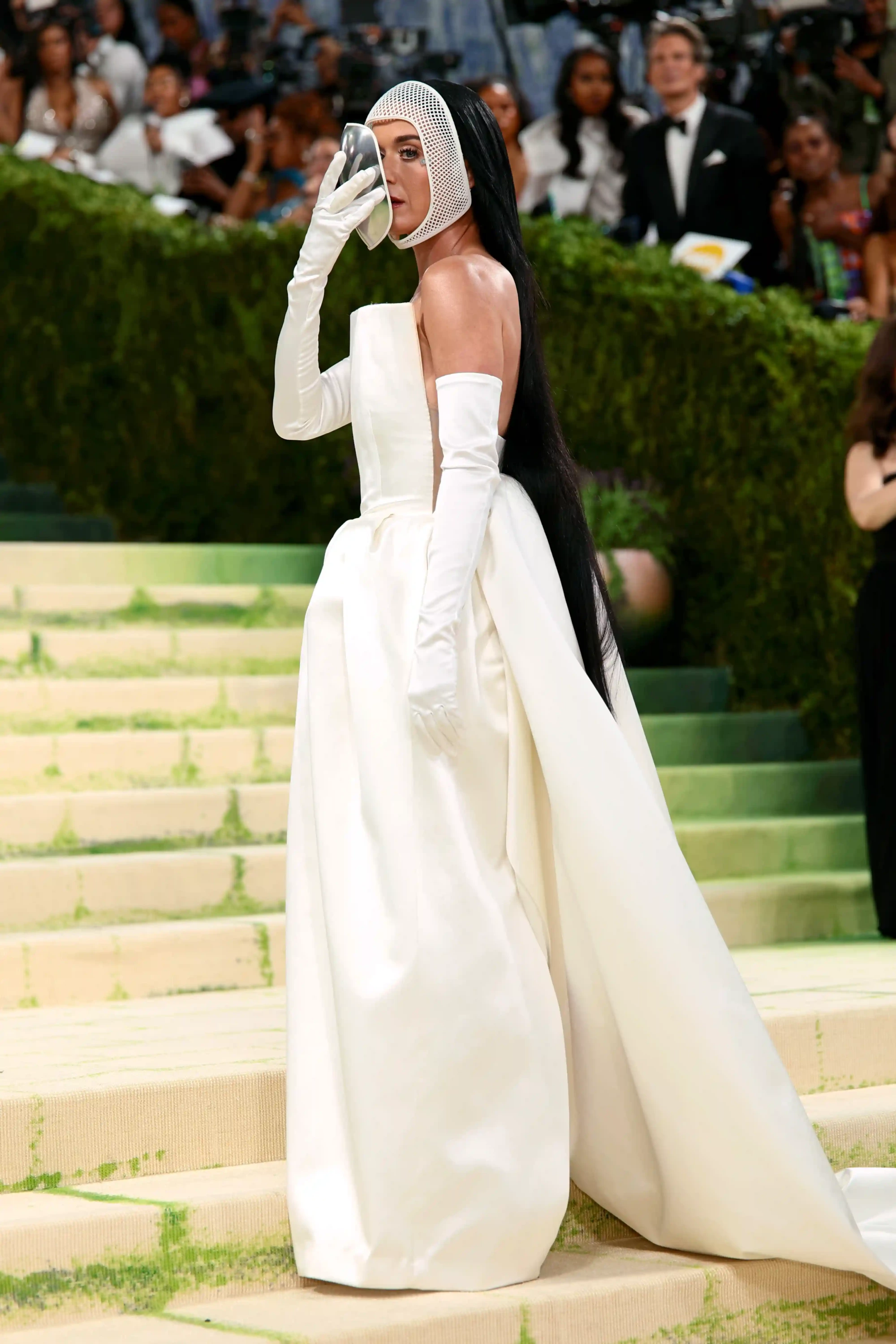 Katy Perry, Fashion is Art temalı 2026 Met Gala kırmızı halısında, bembeyaz, kabarık etekli straplez bir elbise, zarif uzun eldivenler ve başındaki file maskeyle uyumlu, yüzünü kısmen kapayan metalik bir aksesuarla, moda ve sanat arasındaki ilişkiyi vurgulayan iddialı bir kostümle dikkat çekiyor.