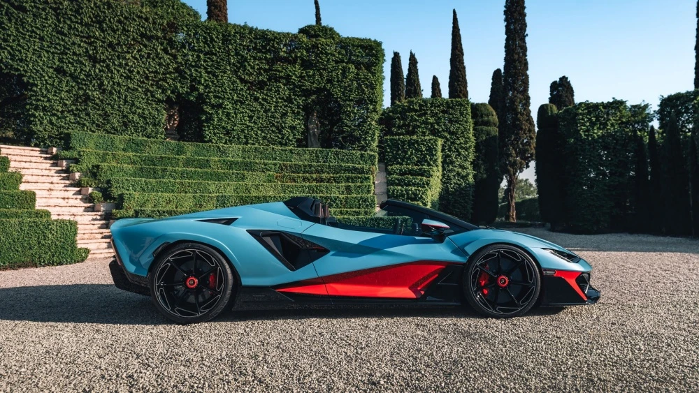Görkemli İtalyan bahçesinde, açık mavi ve kırmızı renkleriyle öne çıkan Lamborghini Fenomeno Roadster, yan profilden çekilmiş bu karede keskin hatlara sahip dinamik tasarımıyla dikkat çekerek modern ve lüks estetiğini gözler önüne seriyor.