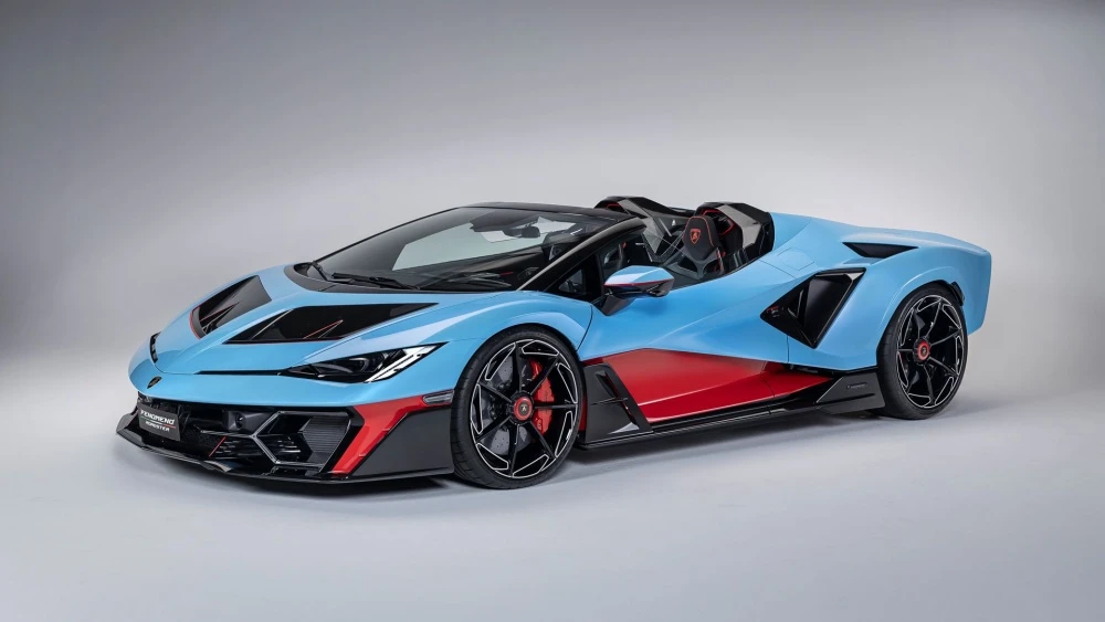 Geniş açıyla görünen, açık mavi ana renge ve yanlarda belirgin kırmızı vurgulara sahip fütüristik Lamborghini Fenomeno Roadster modelinin stüdyo çekimi, dinamik ön tasarımını ve üstü açık yapısını sergiliyor.