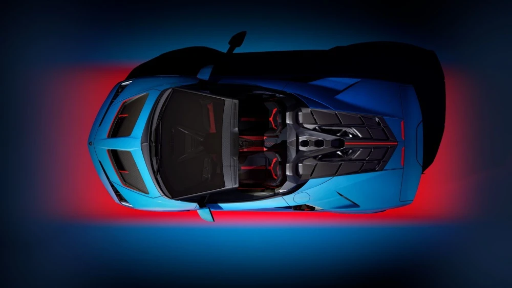 Parlak mavi renkli, üstü açık bir Lamborghini Fenomeno Roadster'ın kuşbakışı görünümü, aracın kırmızı detaylı iç tasarımını ve arkadaki güçlü motor bölümünü vurgularken, koyu mavi zemin üzerindeki dinamik kırmızı ışık çizgisi hız ve performansı çağrıştırıyor.