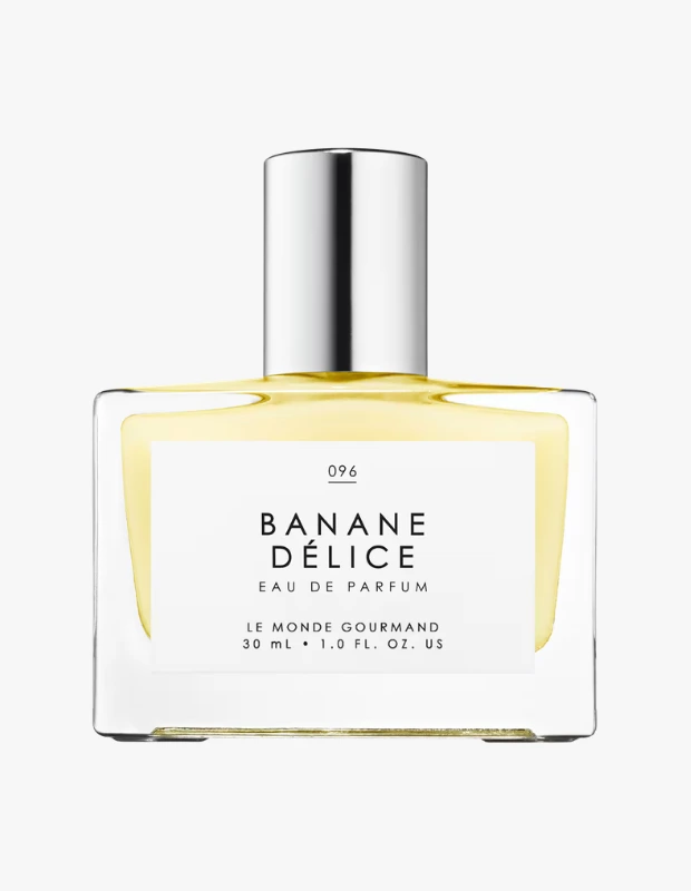 Beyaz arka plan üzerinde duran, şeffaf dikdörtgen cam şişeli ve parlak gümüş renkli kapağı olan bu parfüm, Le Monde Gourmand markasına ait Banane Délice Eau de Parfum'u sergiliyor; şişenin içindeki soluk sarı sıvı ve üzerindeki etiketteki büyük Banane Délice yazısı muz esanslı bu eşsiz kokunun çekiciliğini vurguluyor.