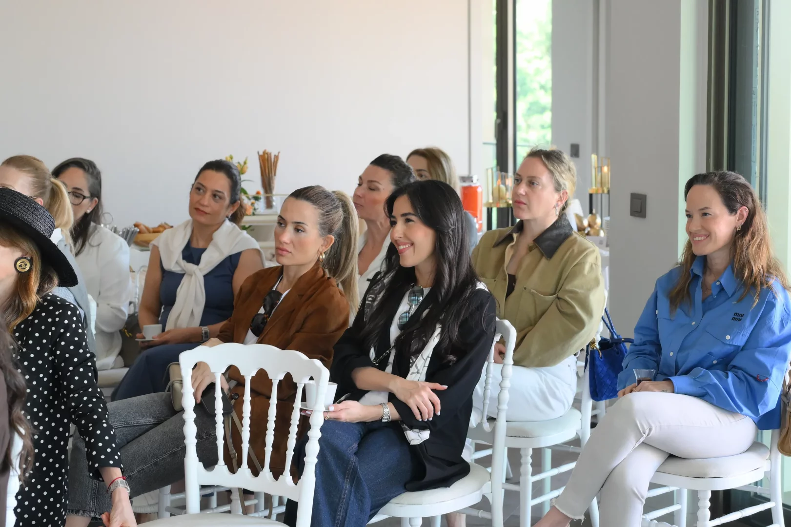 Aydınlık ve modern bir etkinlik alanında, farklı giyim tarzlarına sahip bir grup kadın, Litus İstanbul etkinliğinde konuşmacıları dikkatle dinlerken, bazıları samimi bir tebessümle ortamın keyfini çıkarıyor, genel bir ilgi ve memnuniyet yansıyor.