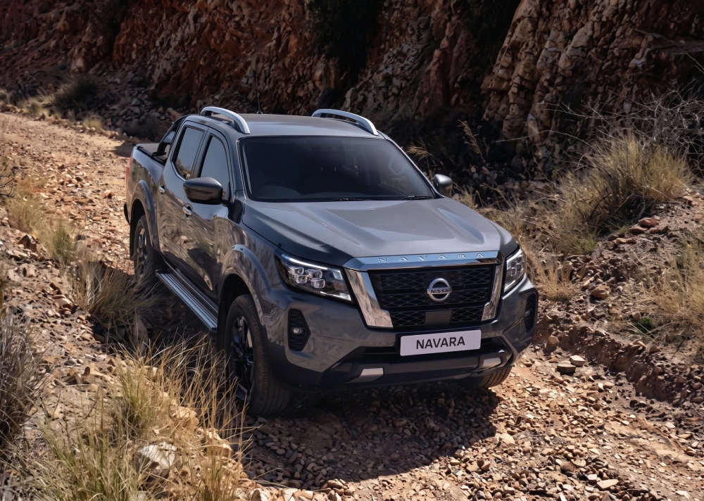 Engebeli ve kayalık bir arazi yolunda, göz alıcı koyu gri renkteki Nissan Navara pickup kamyonet, zorlu koşullara hazır duruşuyla arkasındaki dağlık ve kurak peyzajın içinde offroad yeteneklerini belirgin bir şekilde ortaya koyuyor.