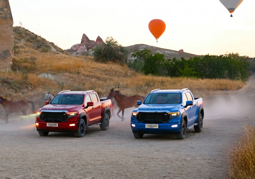 Kapadokya'nın eşsiz coğrafyasında, tozlu bir off-road yolda ilerleyen kırmızı ve mavi iki Otokar Foton Tunland V9 pickup, etraftaki atlar ve gökyüzündeki sıcak hava balonuyla büyüleyici bir manzara sunuyor.