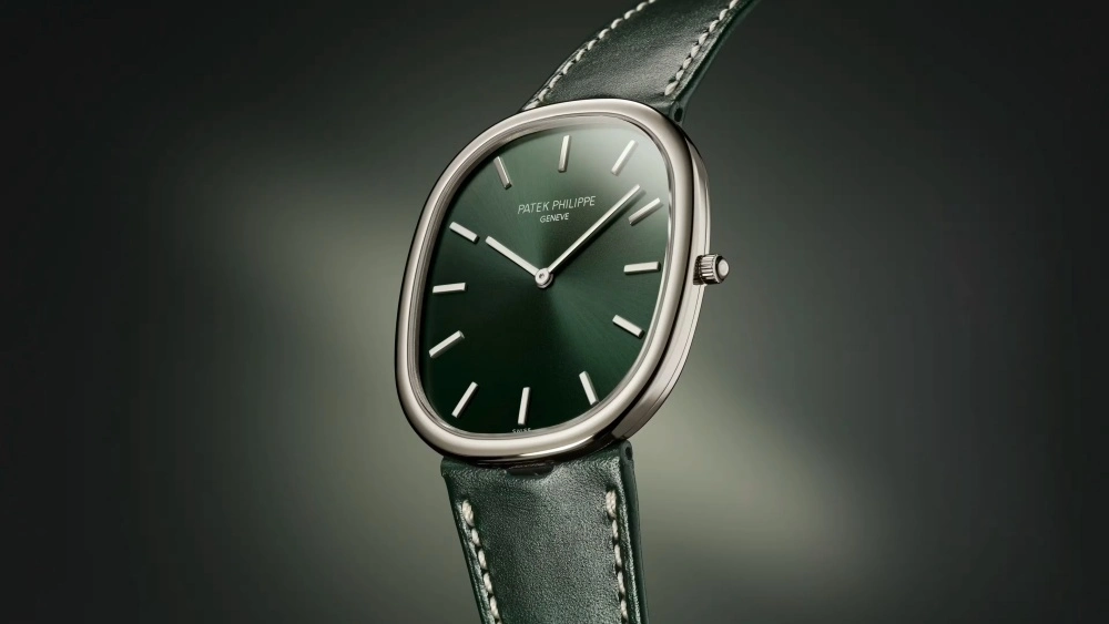 Koyu, zarif bir fon üzerinde açılı bir şekilde konumlandırılmış olan bu Patek Philippe Golden Ellipse modeli, beyaz altın kasası ve güneşte parlayan zümrüt yeşili kadranıyla öne çıkarken, beyaz dikişli zarif yeşil deri kayışı modern ve klasik estetiği mükemmel bir şekilde harmanlıyor.