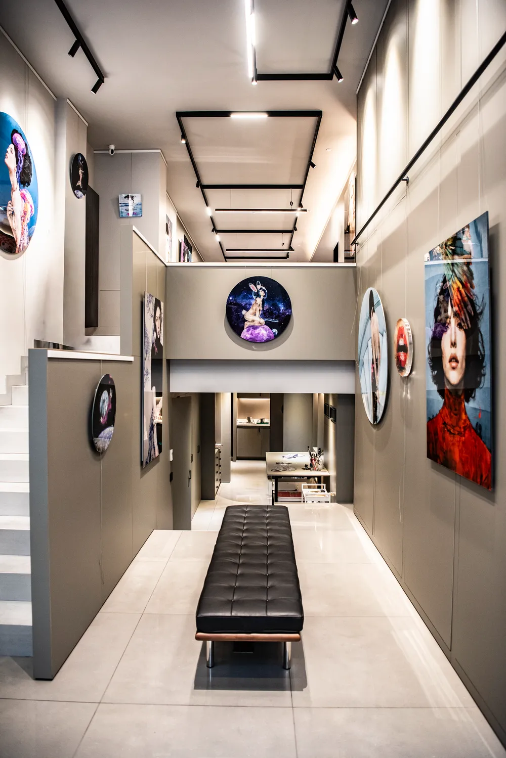 Modern ve yüksek tavanlı bir sanat galerisinde, farklı boyutlarda asılı duran çarpıcı çağdaş eserlerin önünde, ortada şık siyah deri bir bank yer alıyor ve bu aydınlık mekânın Sait Mingu'nun estetik anlayışını yansıttığı izlenimi veriyor.