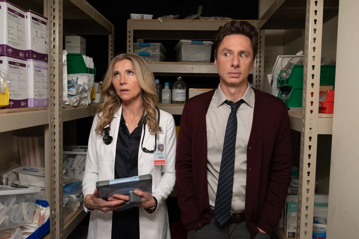 Hastanenin tıbbi malzeme deposunda, doktor önlüklü bir kadın ve kravatlı, bordo hırkalı Zach Braff'ın şaşkın ifadelerle yukarı baktığı, etraflarında tıbbi eldiven kutuları ve IV serum şişelerinin bulunduğu, bir anlık gerilimin hissedildiği bir görsel.