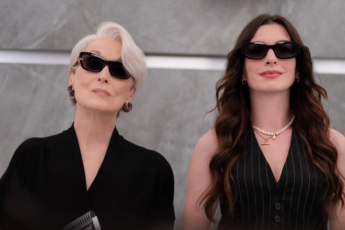 Şeytan Marka Giyer filminden ikonik güneş gözlükleriyle şık ve kararlı bir duruş sergileyen Miranda Priestly, gri kısa saçları ve siyah üstüyle sol tarafta; Andy Sachs ise uzun kahverengi saçları, incili kolyesi ve çizgili yeleğiyle sağ tarafta yer alıyor.