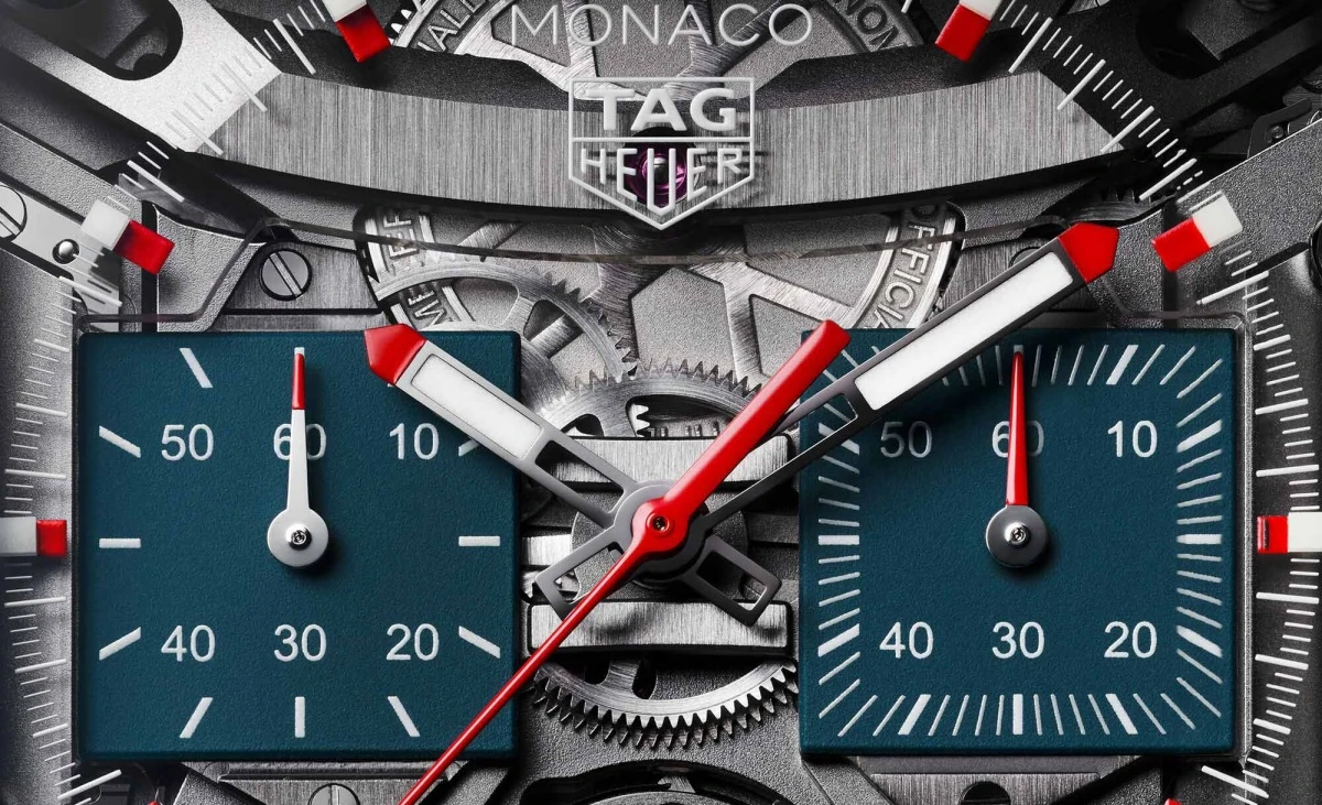 Görselde, Tag Heuer Monaco kronograf saatinin karmaşık iskelet kadranına yakın çekim görülüyor; mekanizmanın dişlileri, koyu mavi kare alt kadranları, kırmızı ibreleri ve markanın logosu detaylarıyla dikkat çekiyor.