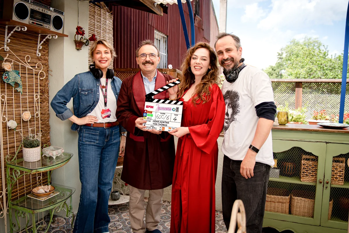 Aile Arasında filminin setinden ilk karelerde, yönetmen Ozan Açıktan'ın adı yazılı bir klaketi neşeyle tutan bir kadın oyuncu ve diğer üç set ekibi üyesi, yeşilliklerle çevrili renkli bir ortamda kameraya içtenlikle gülümsüyor.