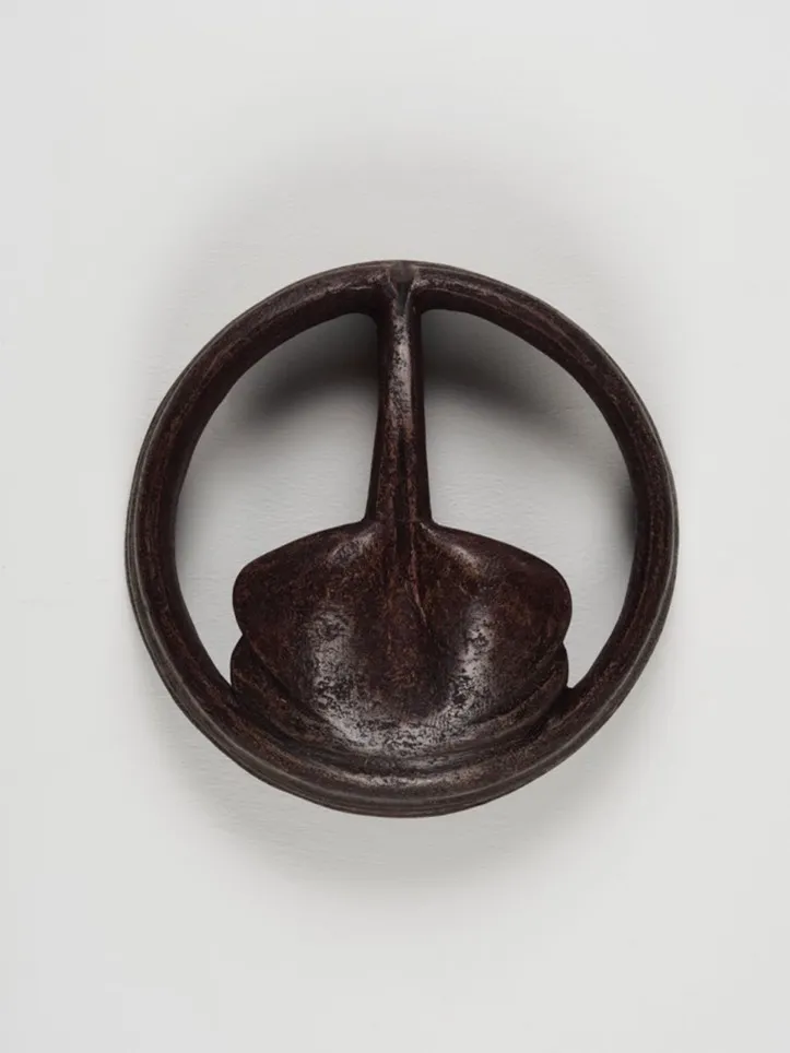 Art Basel'de görülmesi gerekenler arasında yer alan bu koyu kahverengi, dokulu metal sanat eseri, ortasında oval bir halka bulunan ve alt kısmında stilize edilmiş organik bir formla birleşen soyut bir heykeli sergiliyor.