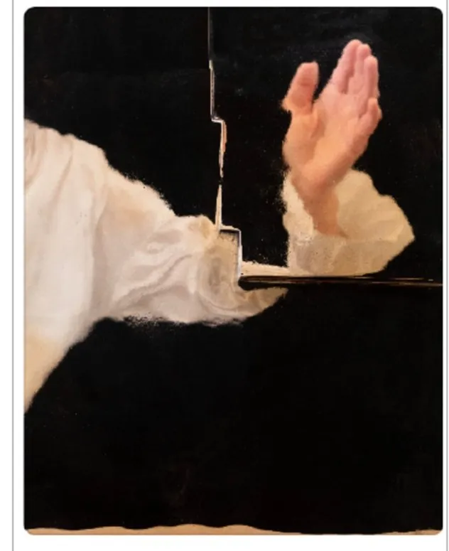 Art Basel'de görülebilecek etkileyici eserlerden biri olan bu sanatsal çalışmada, karanlık arka planın önünde, sol tarafta beyaz, kabarık bir kolun detayı ve sağ tarafta yukarı doğru uzanan soluk renkli bir elin dinamik pozu, düşündürücü bir ayrım çizgisiyle bölünmüş olarak yer alıyor.