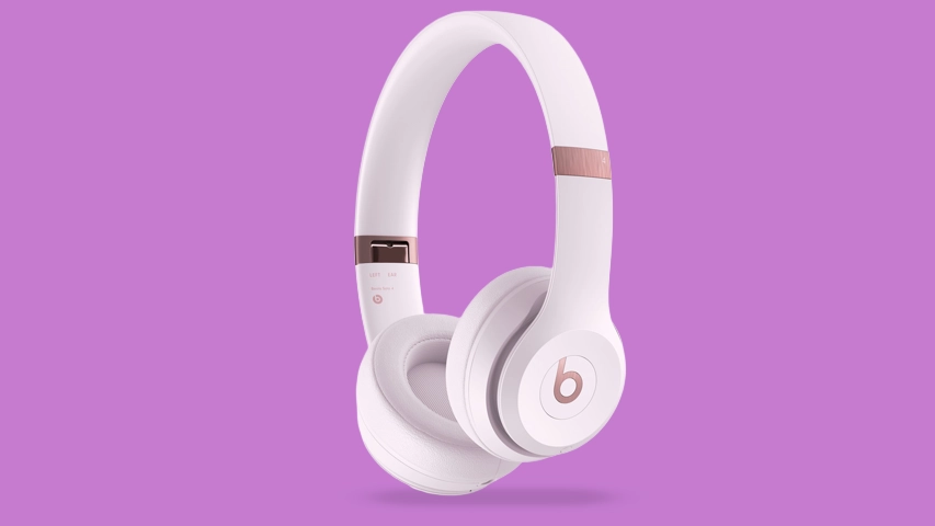 Mor renkte sade bir arka plan önünde, sağ tarafı hafifçe öne eğik konumda duran, mat beyaz kulaklık yastıkları ve kafa bandına sahip, rose gold detaylı Beats logosu ve metalik ayar noktalarıyla şık bir Beats Solo 4 kablosuz kulaklık modeli gösterilmektedir.
