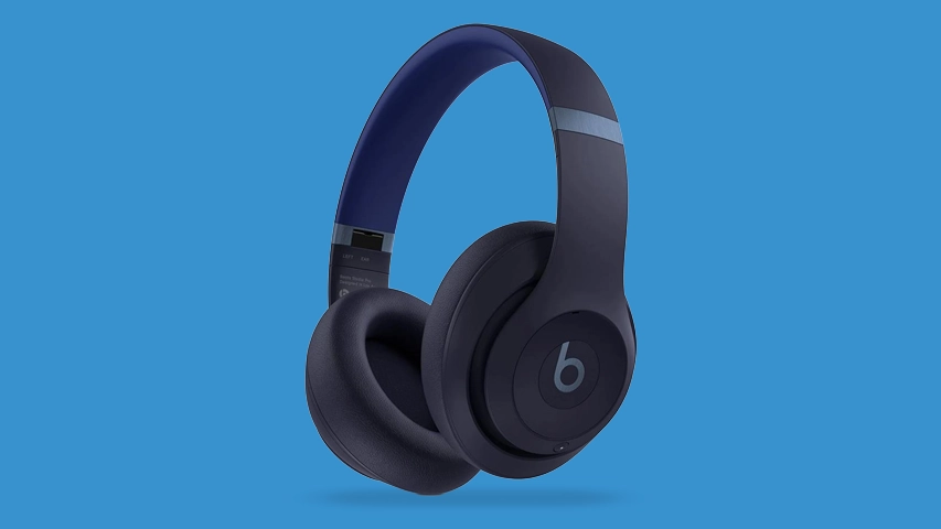 Bir Beats Studio Pro kulaklık, lacivert renginde, kulak yastıkları ve kafa bandı detayları net bir şekilde görünürken, parlak mavi bir zeminde havada duruyormuş gibi hafif bir gölgeyle sergileniyor.